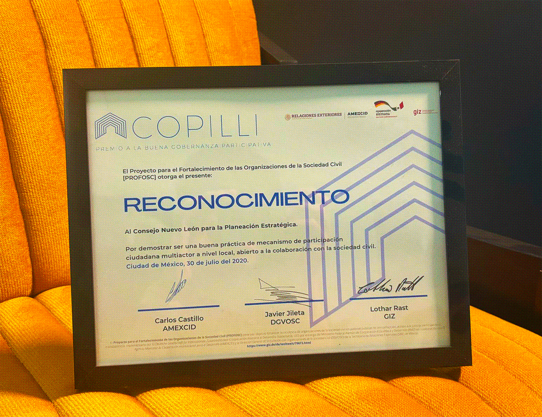 Un reconocimiento enmarcado, el Premio Copilli, arriba de un sillón amarillo.