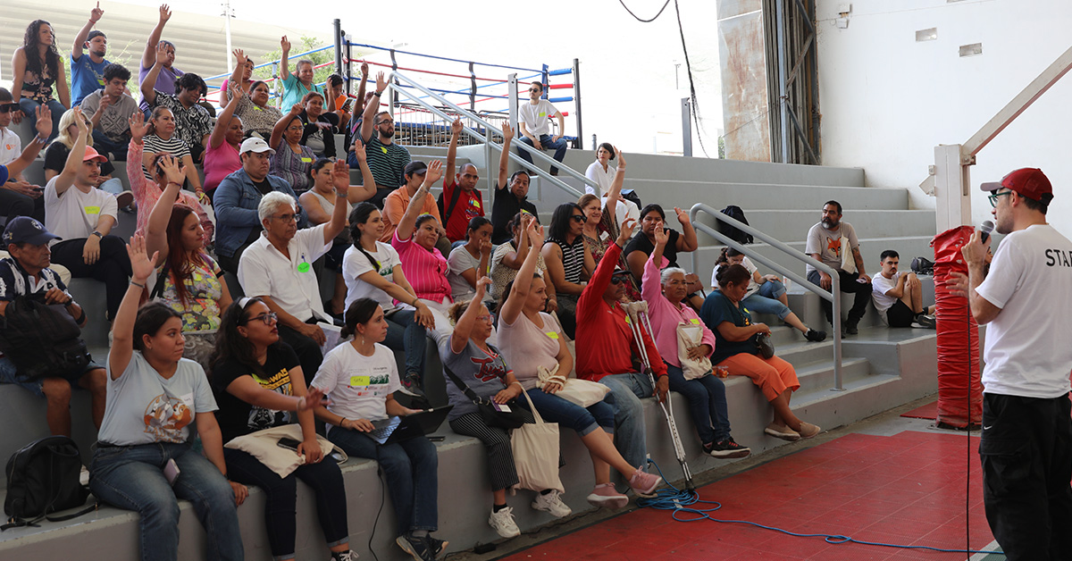 Personas votando en un auditorio levantando las manos.